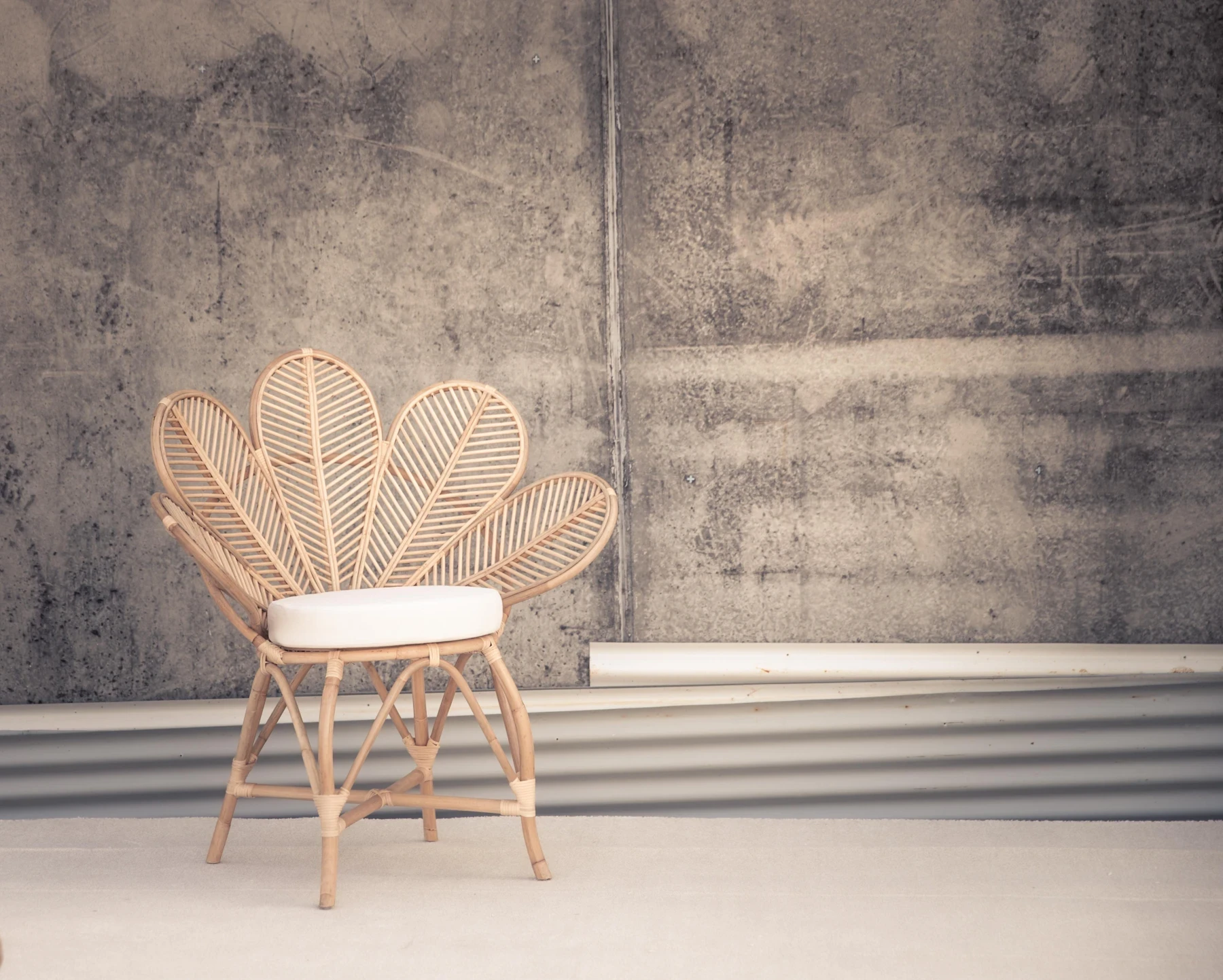 Chaise en rotin aux lignes arrondies devant un mur gris texturé.