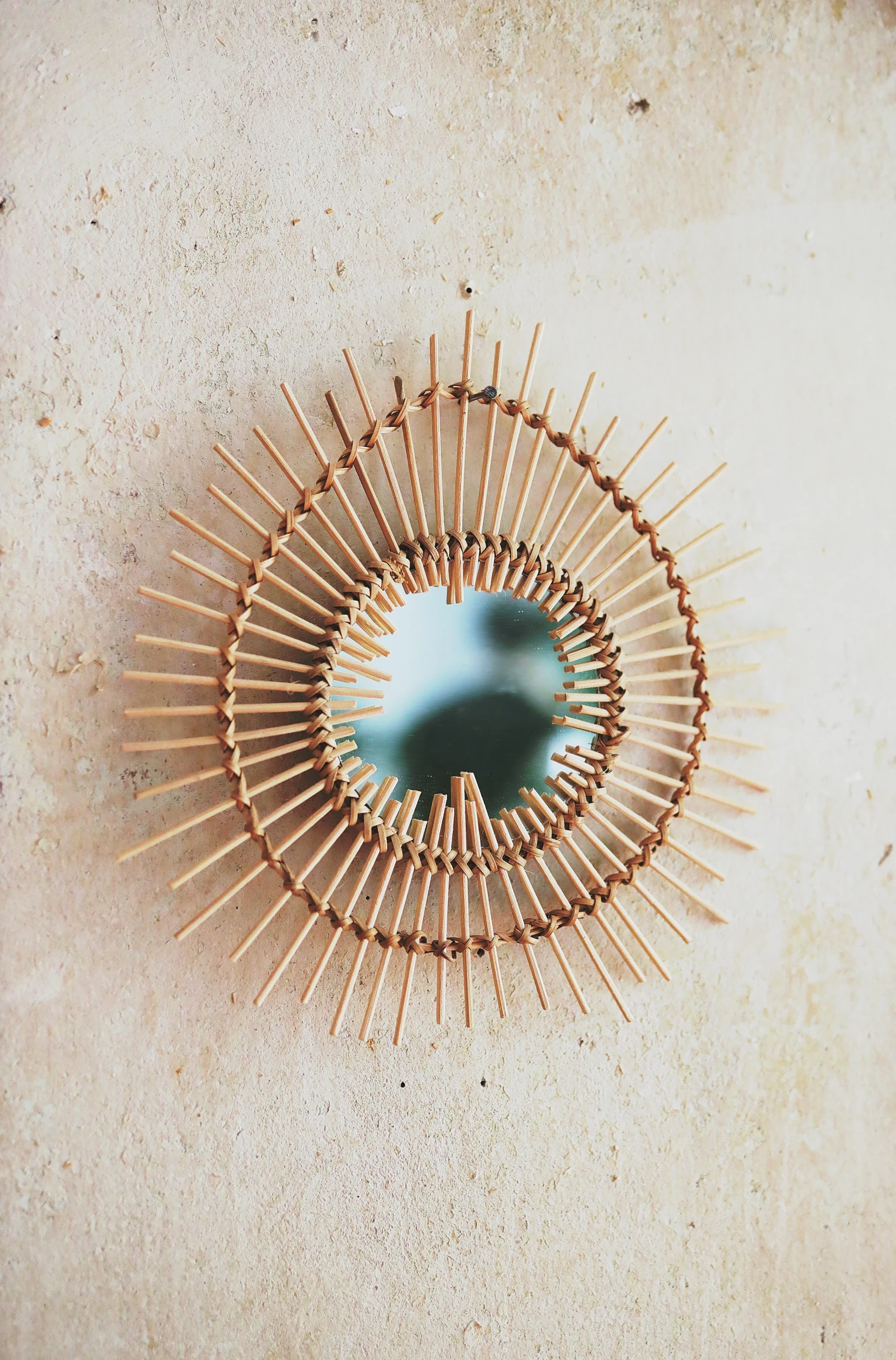 Miroir rond encadré de rayons en rotin sur un mur clair.